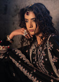 Woman wearing an embroidered black outfit with jewelry against a neutral background