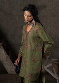 Woman wearing a green embroidered outfit in a dimly lit room.