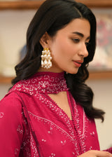 Woman wearing a pink embroidered outfit with gold earrings indoors