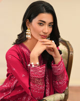 Woman wearing a pink traditional outfit with intricate patterns, sitting on a chair.