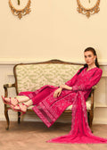 Woman in a bright pink traditional outfit sitting on an ornate couch in a decorated room.