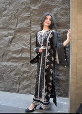Woman wearing a black and white embroidered dress against a stone wall.