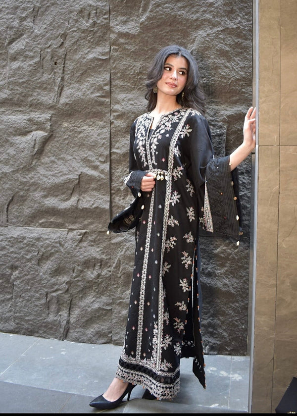 Woman wearing a black and white embroidered dress against a stone wall.