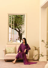 Woman in a purple outfit sitting on a couch in a room with a large mirror reflecting a tree.