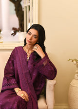 Woman in a purple embroidered outfit sitting on a white chair indoors.