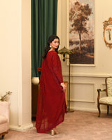 Woman in a red outfit standing in an elegant room with a painting and lamp in the background.