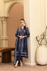 Woman in a blue patterned dress standing in an elegant interior setting.