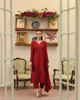 Woman in a red outfit standing in a room with decorative shelves and chairs.