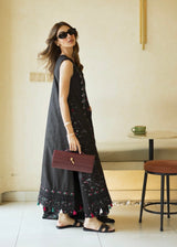 Woman in a long dark dress with floral patterns standing in a modern interior setting.