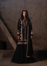 Woman wearing a black embroidered dress against a textured wall.
