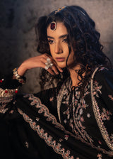 Woman wearing an embroidered black outfit with jewelry against a neutral background