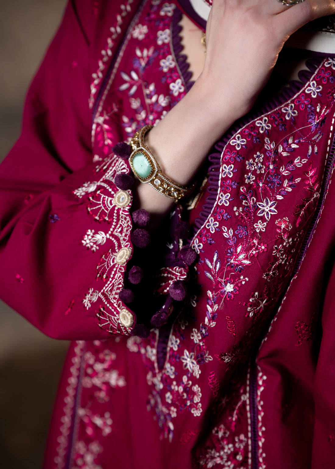 Woman wearing a magenta embroidered outfit against a dark background
