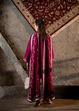 Woman in a long, patterned dress standing in a room with a textured wall and decorative rug.