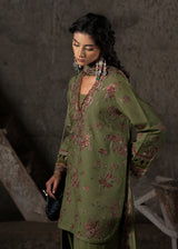 Woman wearing a green embroidered outfit in a dimly lit room.