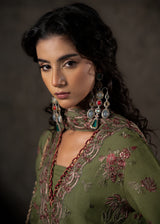 Woman wearing an embroidered green traditional outfit with jewelry against a dark background