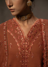 Close-up of a person wearing an intricately embroidered brown garment with a dark background