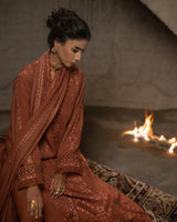 Woman in a brown embroidered outfit sitting by a fire