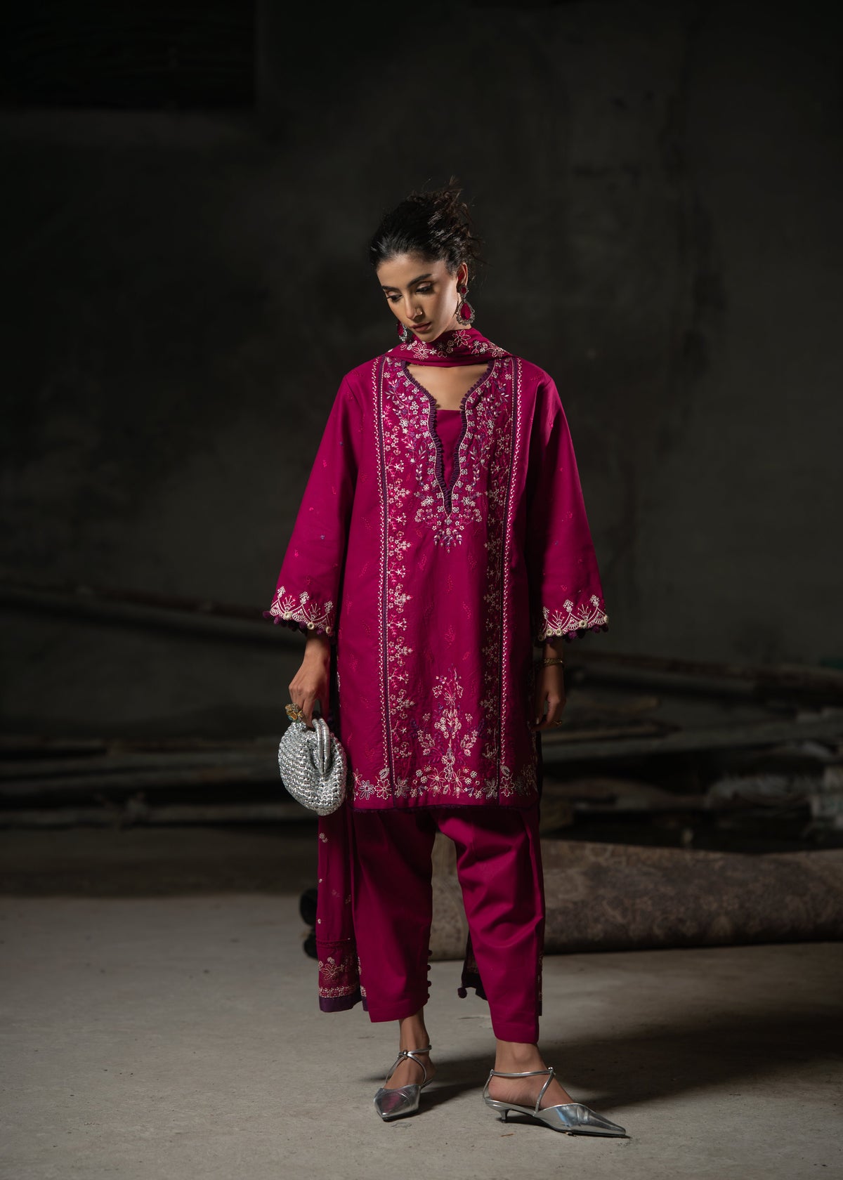 Woman wearing a magenta embroidered outfit against a dark background