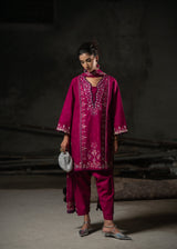 Woman wearing a magenta embroidered outfit against a dark background