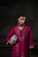 Woman in a magenta embroidered outfit holding a clutch against a dark background