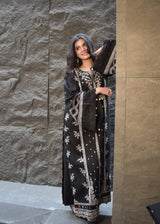 Woman wearing a black and white embroidered dress against a stone wall.