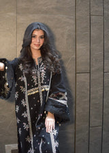 Woman wearing a black embroidered dress against a gray wall
