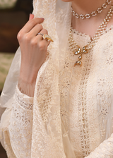 Close-up of a person wearing a white embroidered outfit with jewelry, including a necklace and ring.