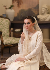 Woman in a white traditional outfit with a veil sitting in an elegant room.